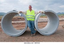 hispanic-worker-standing-near-large-cement-pipes-bn7xg4.jpg